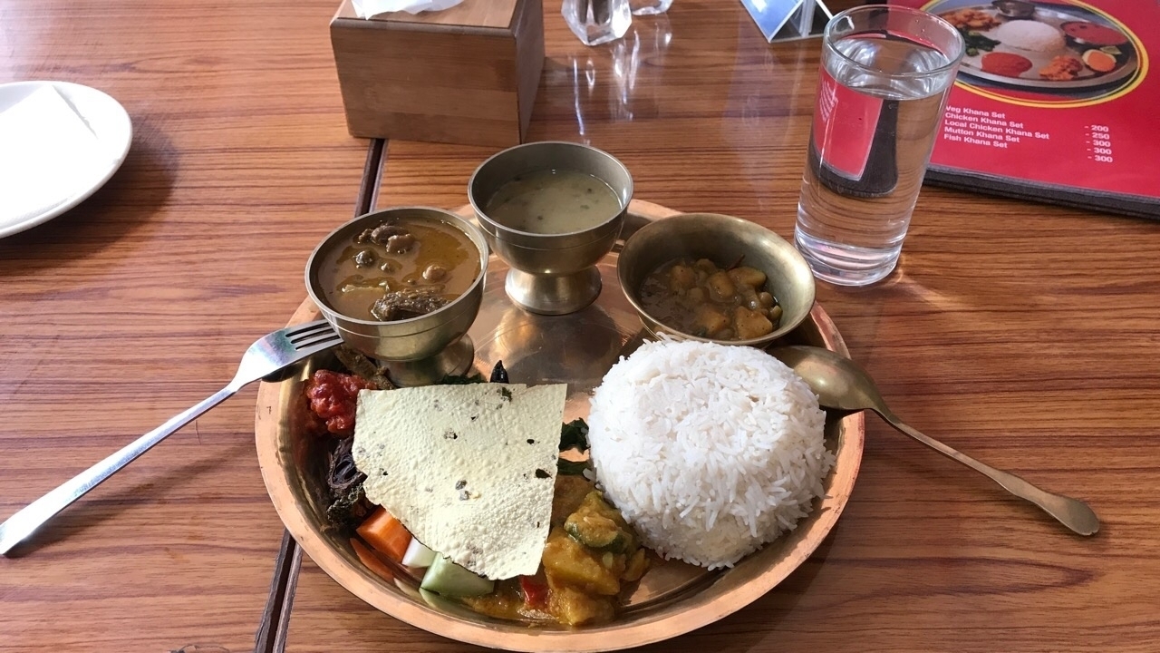 Repas népalais traditionnel servi dans une assiette avec différents plats.