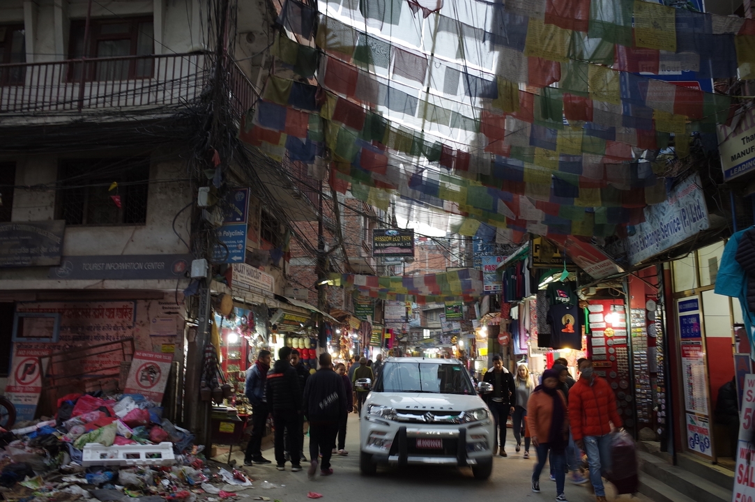 Rue animée à Katmandou avec de nombreux magasins et des drapeaux colorés.