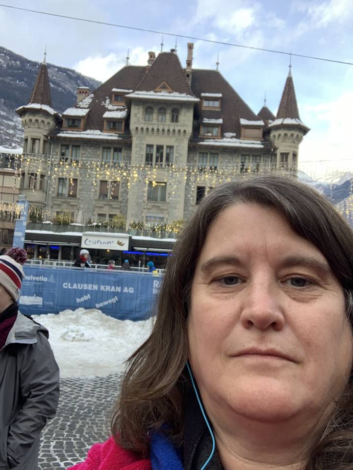 Selfie d'une personne avec un bâtiment couvert de neige en arrière-plan.