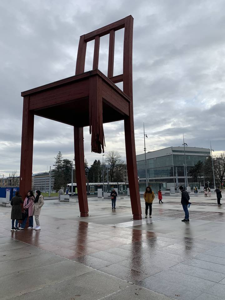 Grande sculpture de chaise brisée dans une place ouverte avec des gens qui se promènent autour.