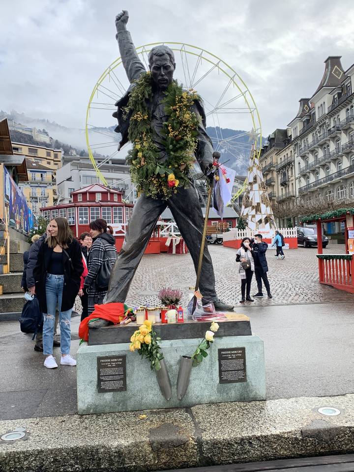 Statue entourée de personnes sur une place publique, avec une grande roue en arrière-plan.