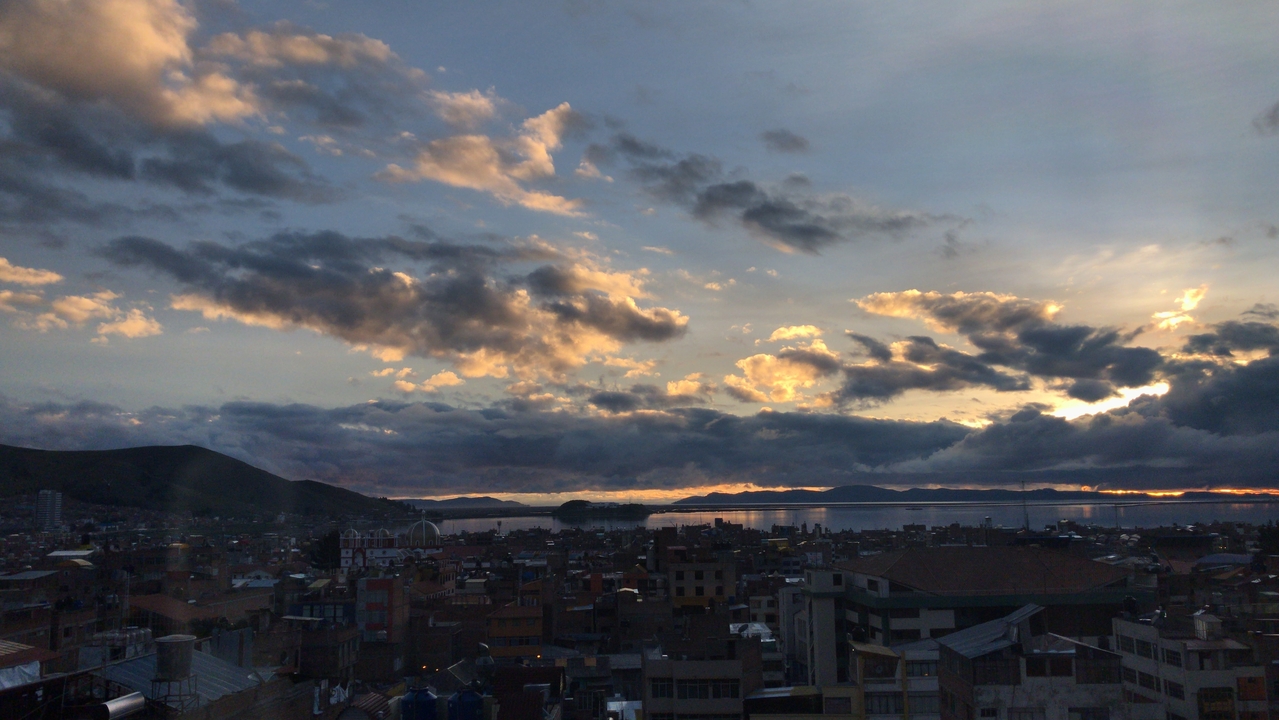 Sunset over a lake with clouds and city skyline.