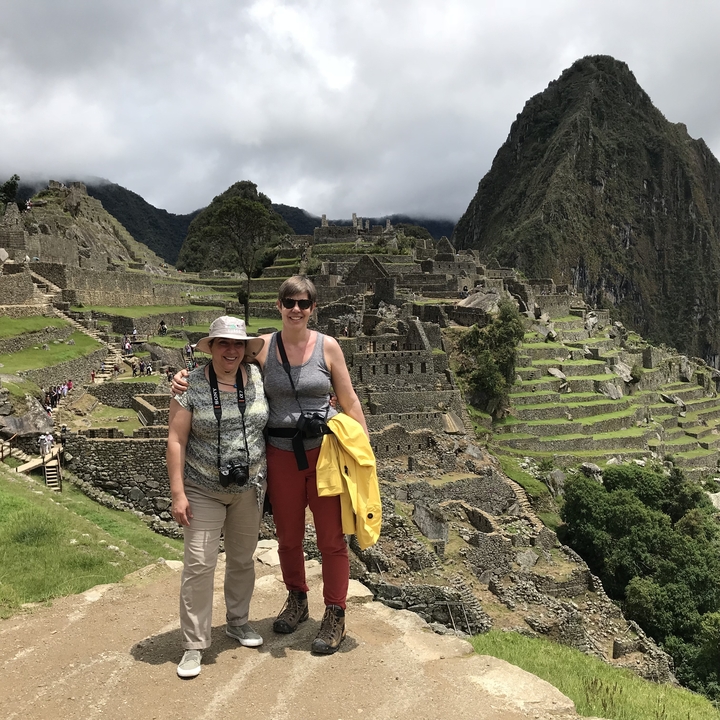 Historic ruins with visitors and dramatic mountain backdrop.