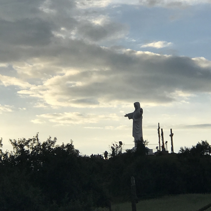 Statue of Christ on a hill with cloudy sky.