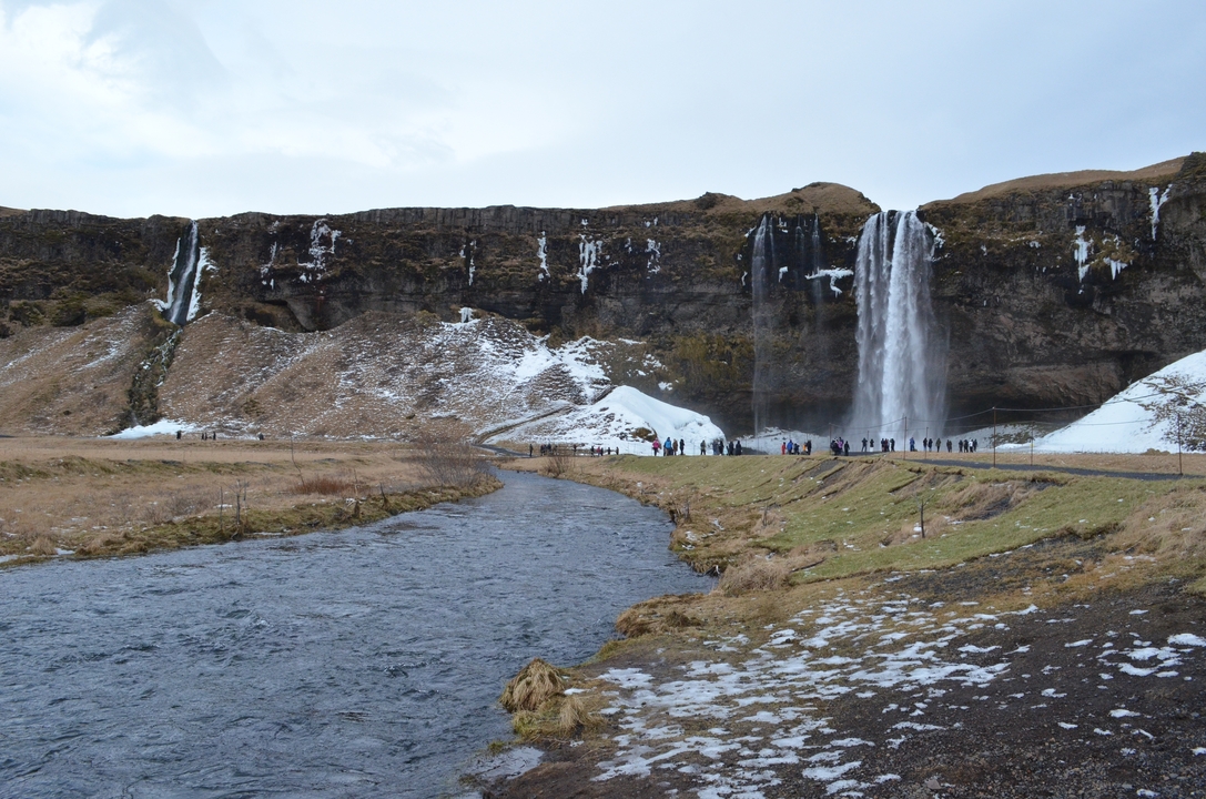Long waterfall with tourists gathering at the base.