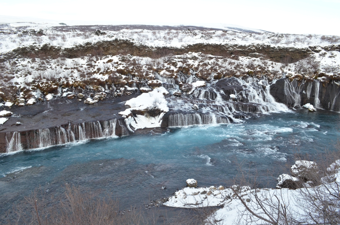 Cascade tombant sur des rochers de basalte noir entourés de neige.