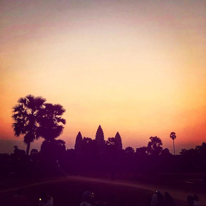 Silhouette de palmiers et de structures de temple au coucher du soleil.
