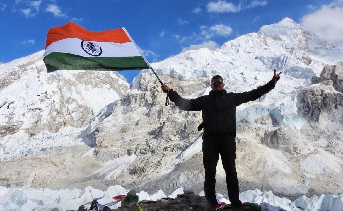 Une personne qui pose avec le drapeau indien devant des montagnes enneigées.