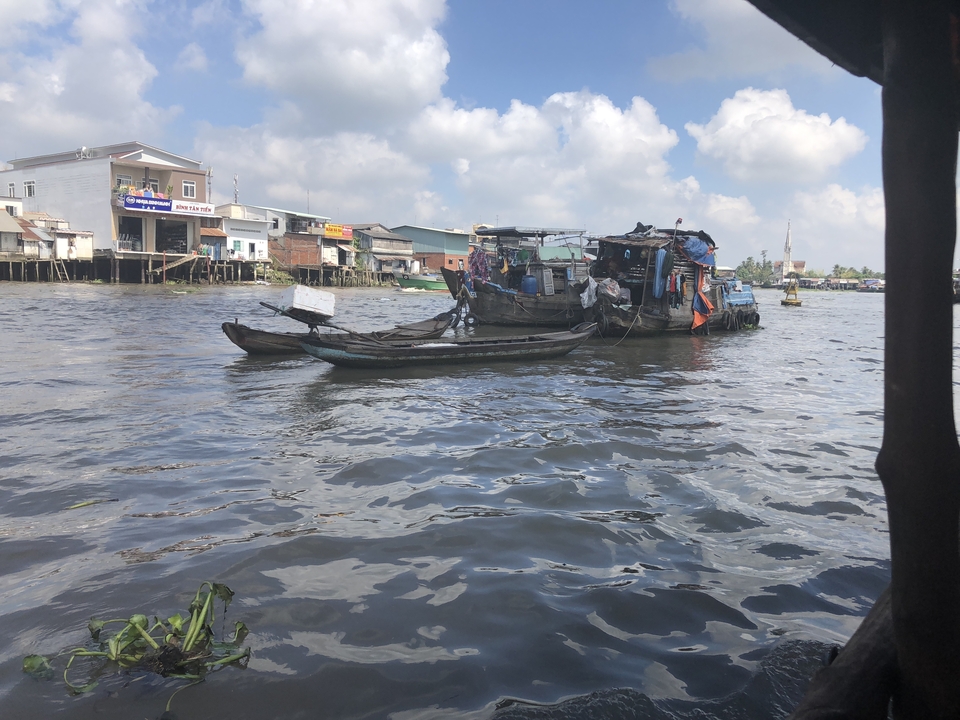 Bateaux sur une rivière avec des maisons sur pilotis le long de la rive.