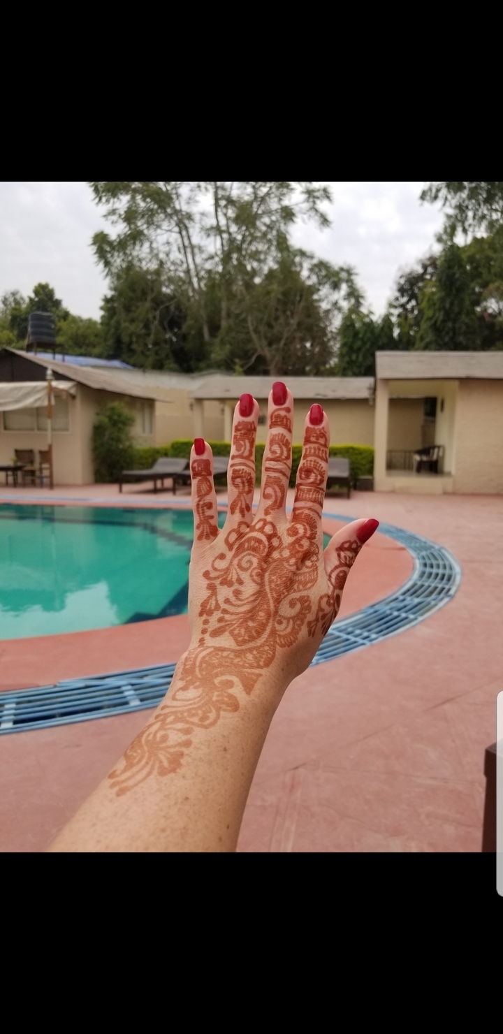 Main avec un motif de henné complexe devant une piscine.
