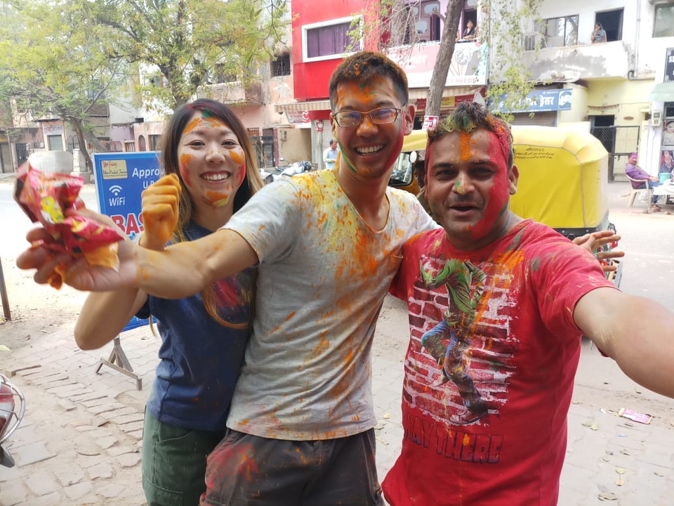Three friends laughing and covered in bright powder during Holi celebrations.