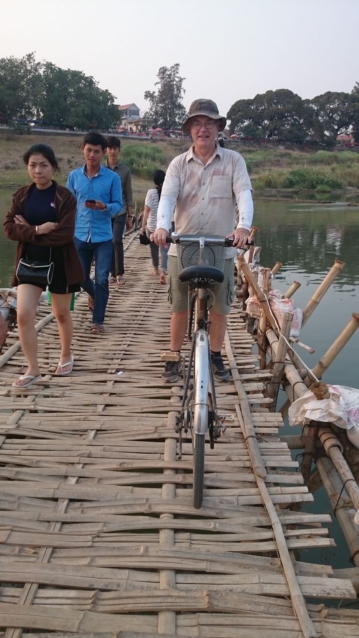 Personne traversant un pont de bambou avec un vélo.