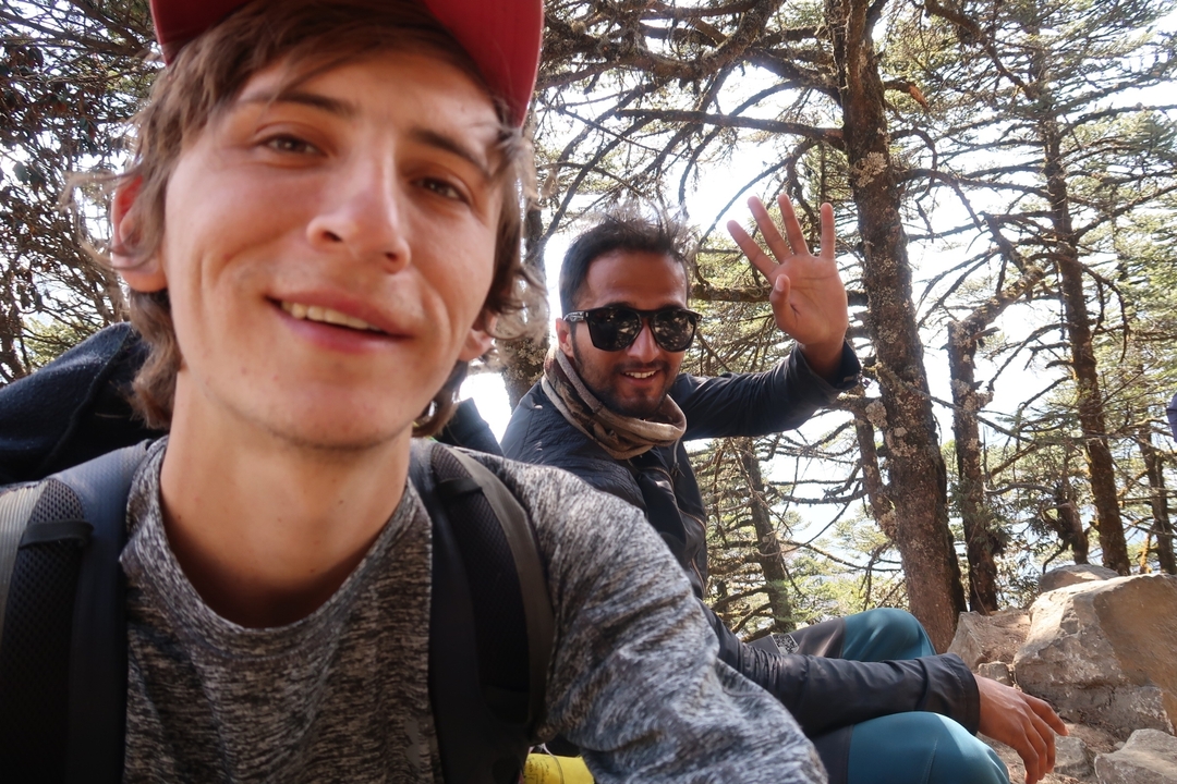 Deux personnes assises parmi les arbres, l'une faisant signe à la caméra.