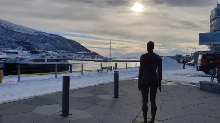 Sculpture of a person overlooking a snowy harbor.