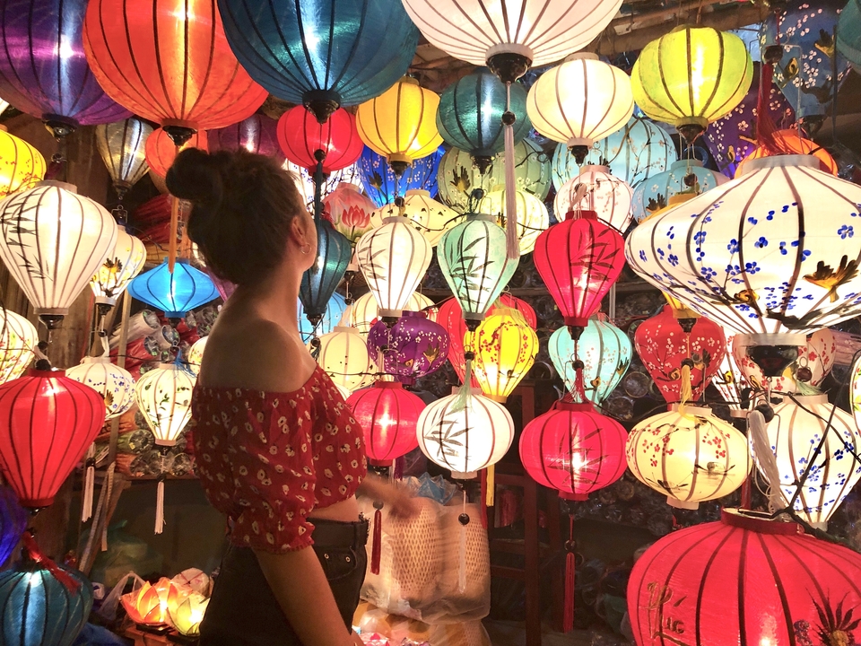 Woman admiring a vibrant display of multicoloured silk lanterns in a night market.