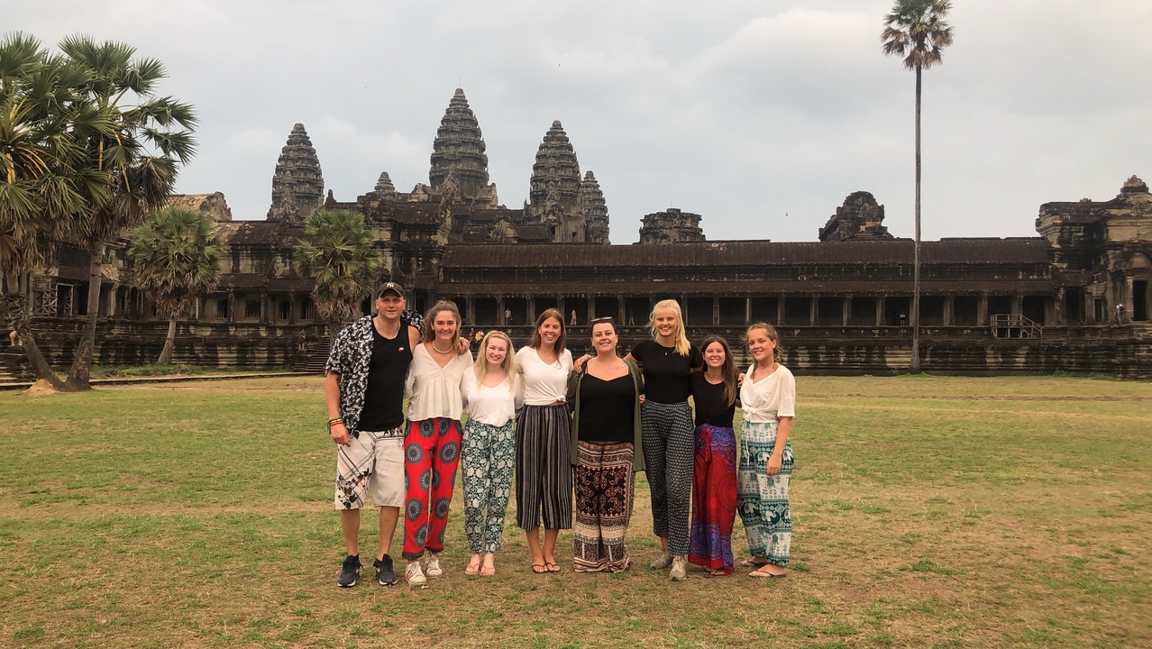 Eight travelers stand together on the lawn in front of the iconic Angkor Wat temple complex.