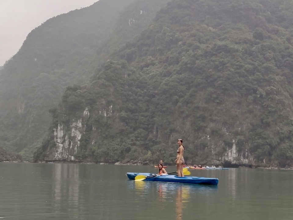Travellers kayaking on calm emerald water surrounded by limestone karsts.