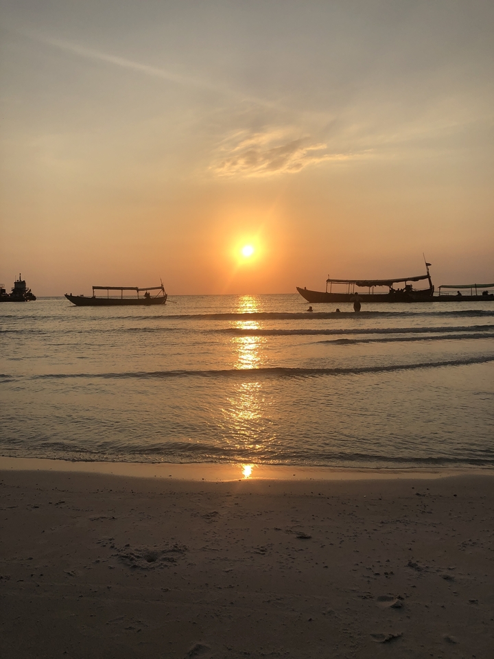 Serene sunset over the ocean with long-tail boats silhouetted against the golden sky.