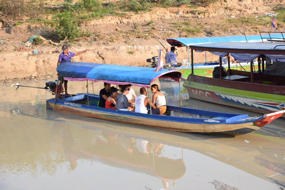 Small motorboat carrying tourists along a muddy river with local guide pointing.