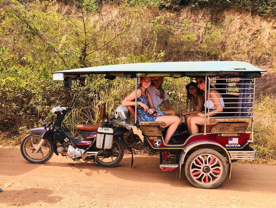 Group of travellers seated in a colourful motorised tuk-tuk on a dusty road.
