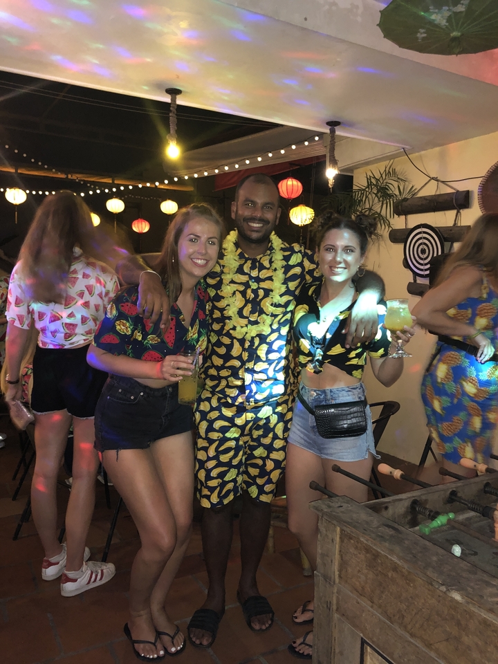 Three friends dressed in bright banana-themed outfits enjoying a party under lantern lights.
