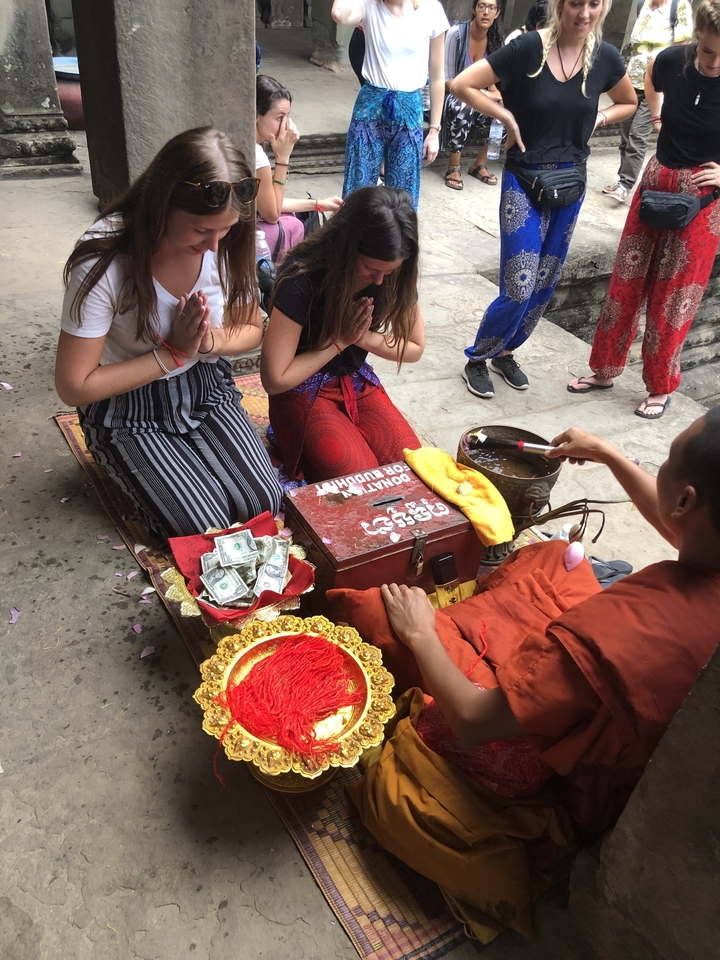 Young travellers kneeling in prayer while a monk performs a blessing ceremony.