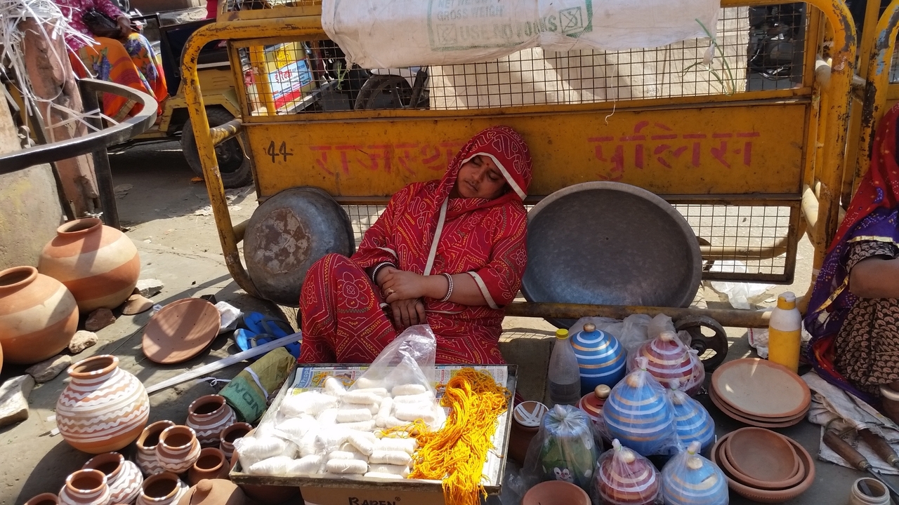 Vendeur de rue se reposant, entouré d'articles de poterie.