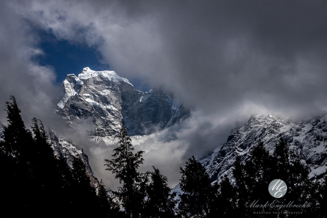 Des montagnes enneigées partiellement obscurcies par les nuages et les arbres.