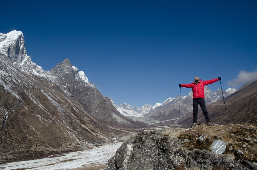 Homme se tenant triomphalement dans une vallée de montagne couverte de neige.
