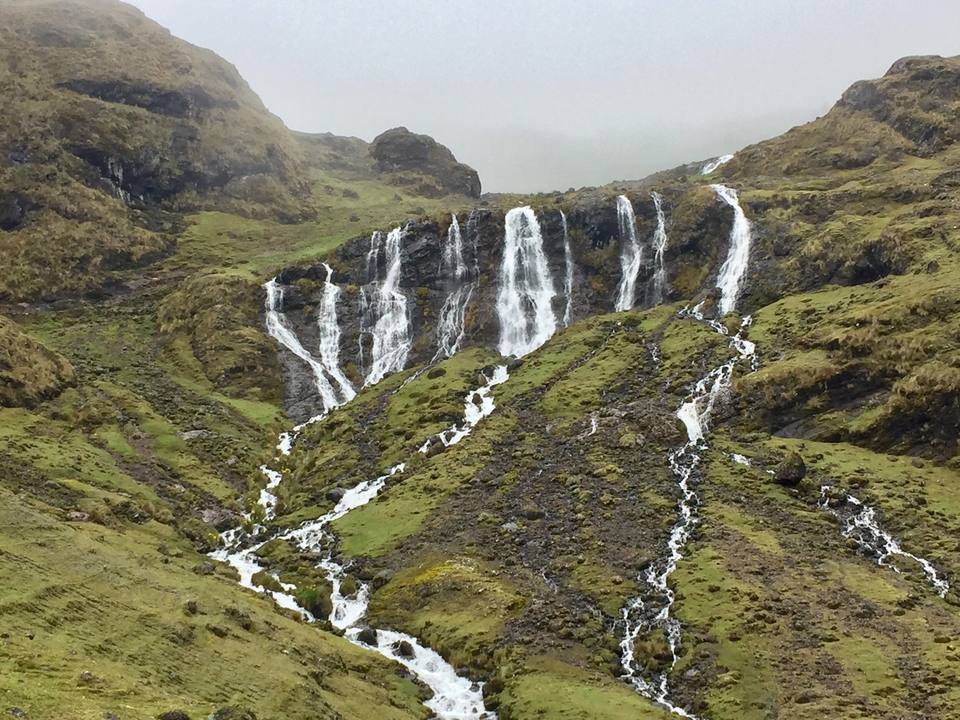 Cascade dévalant le long d'un versant de montagne herbeux.