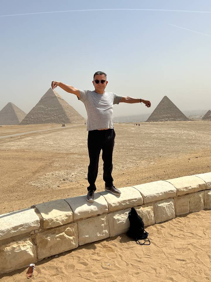 Homme posant les bras étendus devant les Pyramides.