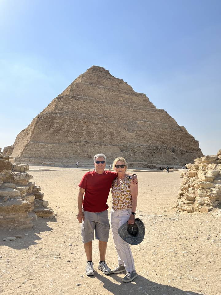 Des touristes debout devant une pyramide à degrés antique.