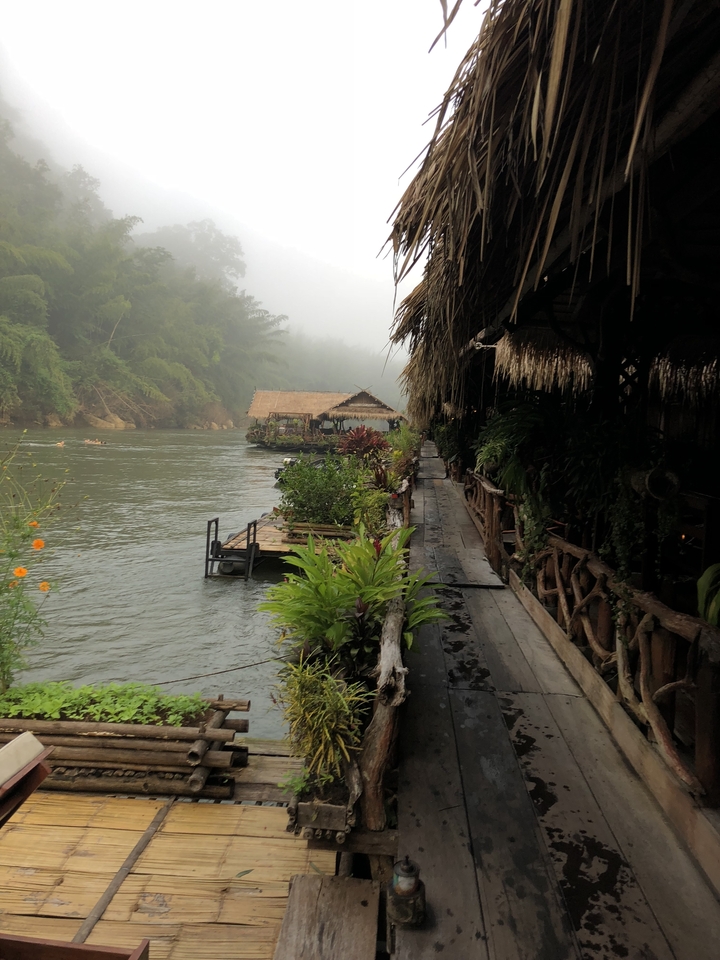 Bord de rivière avec brume et huttes traditionnelles le long d'un sentier.
