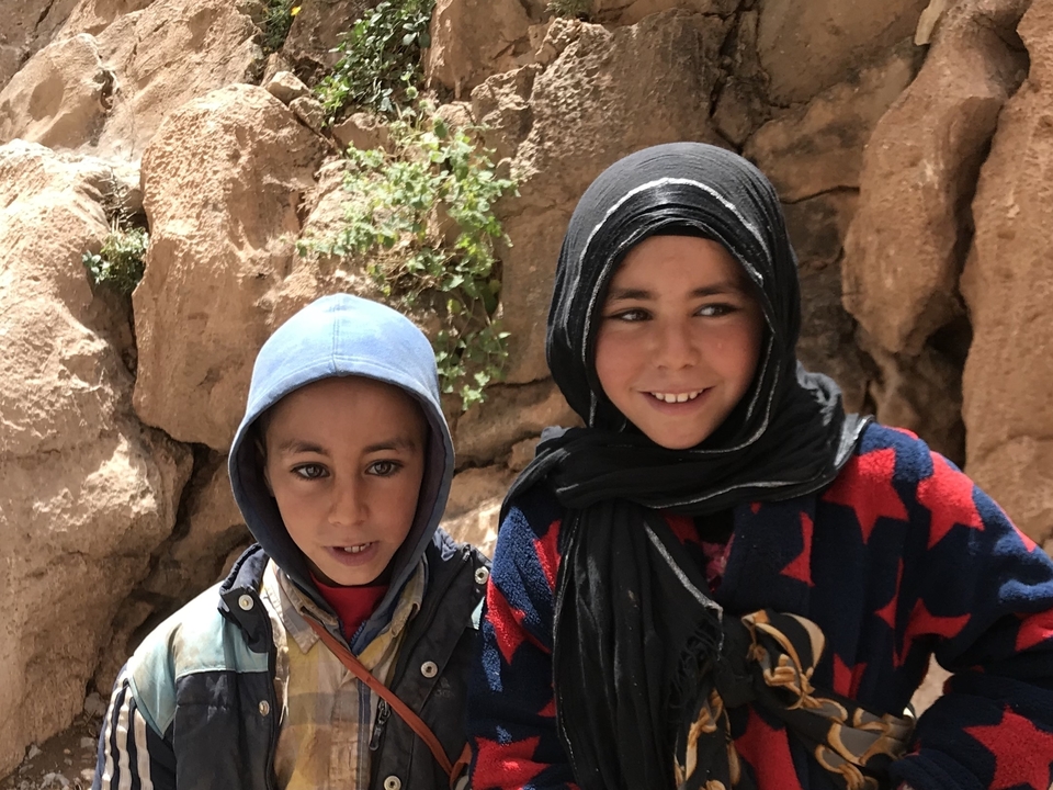 Deux enfants souriants en vêtements traditionnels sur un fond rocheux.