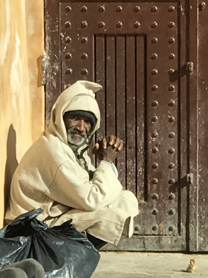 Homme âgé assis devant une porte texturée.