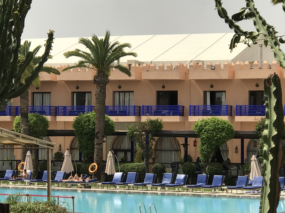 Complexe hôtelier avec palmiers et transats autour d'une piscine.