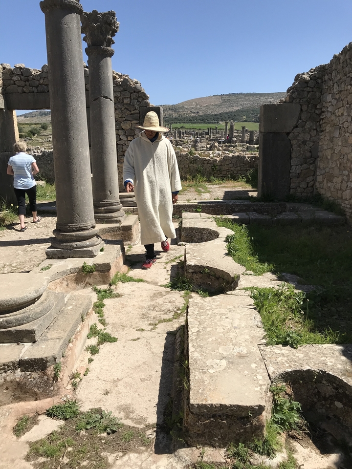 Une personne en costume traditionnel marchant parmi des ruines antiques.