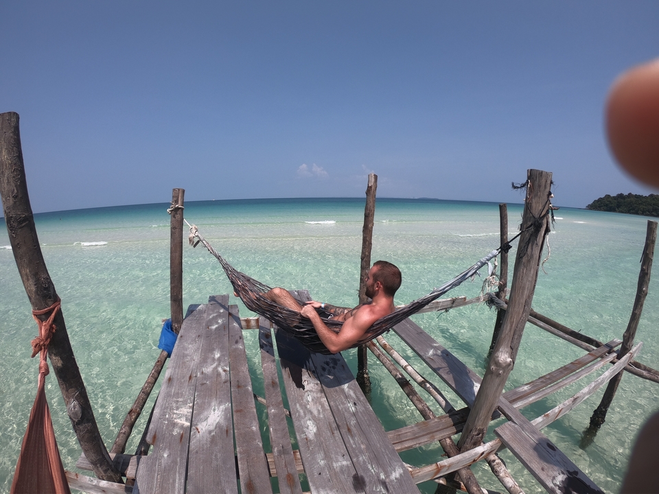 Person relaxing in a hammock over clear water.