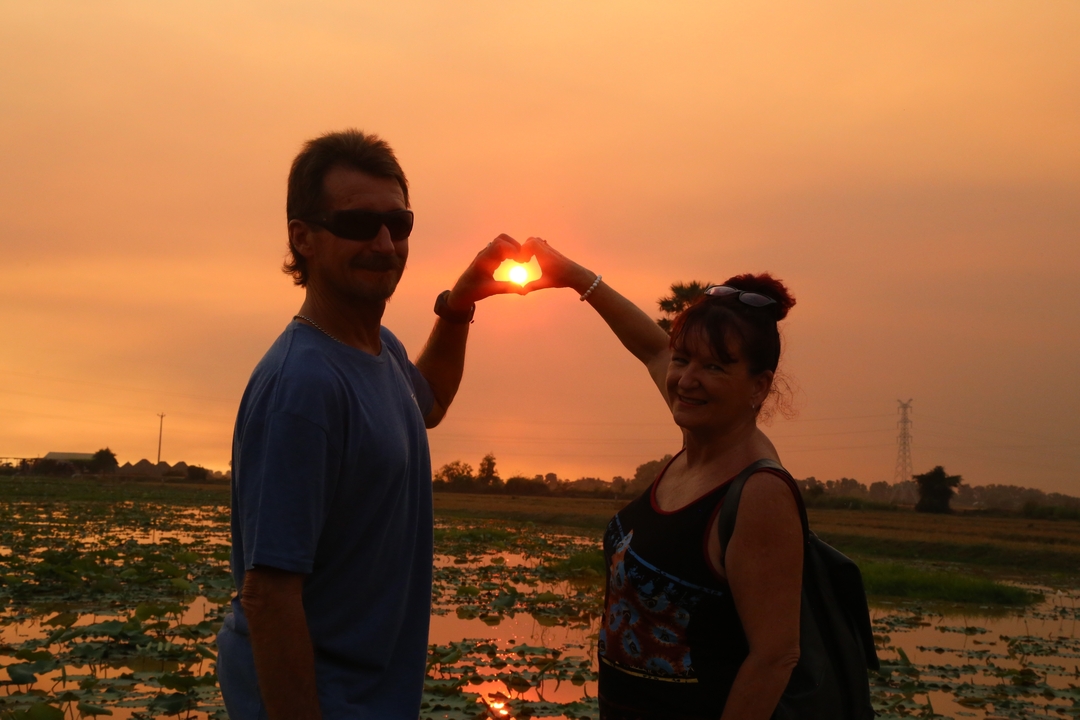 Two people forming a heart shape with their hands around the sunset.