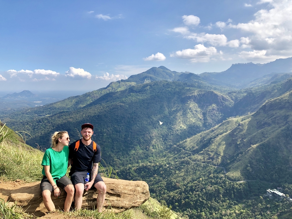 Couple assis sur une falaise avec des montagnes luxuriantes.