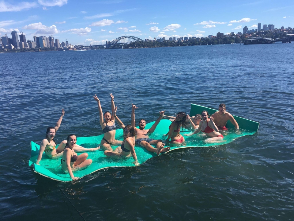 Group of people on a floating device on the water with the Sydney skyline behind.