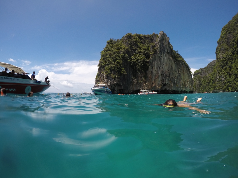 Des gens faisant de la plongée avec tuba près de bateaux et d'une grande falaise calcaire.