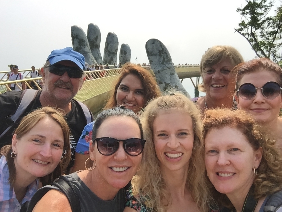 Selfie de groupe sur un pont avec une structure artistique en forme de mains.