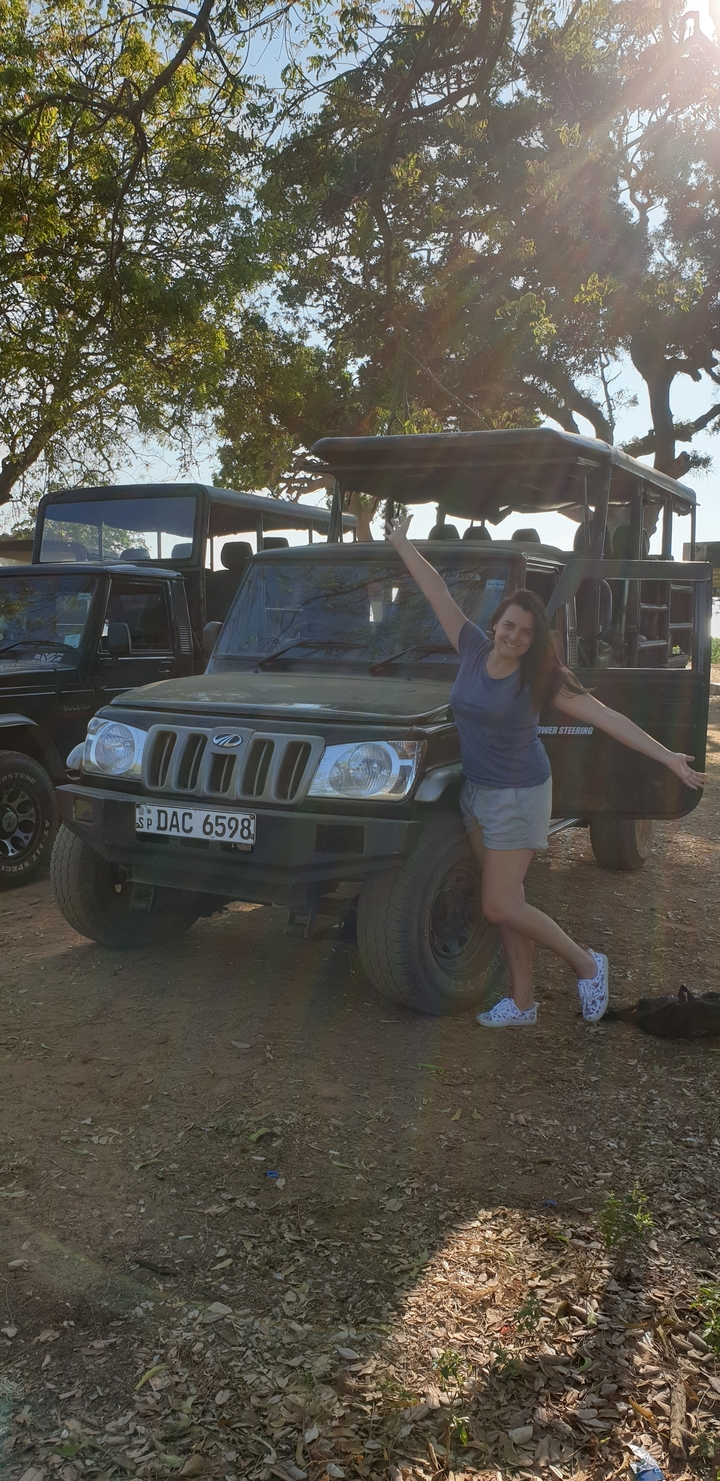 Femme posant énergiquement devant des véhicules de safari.
