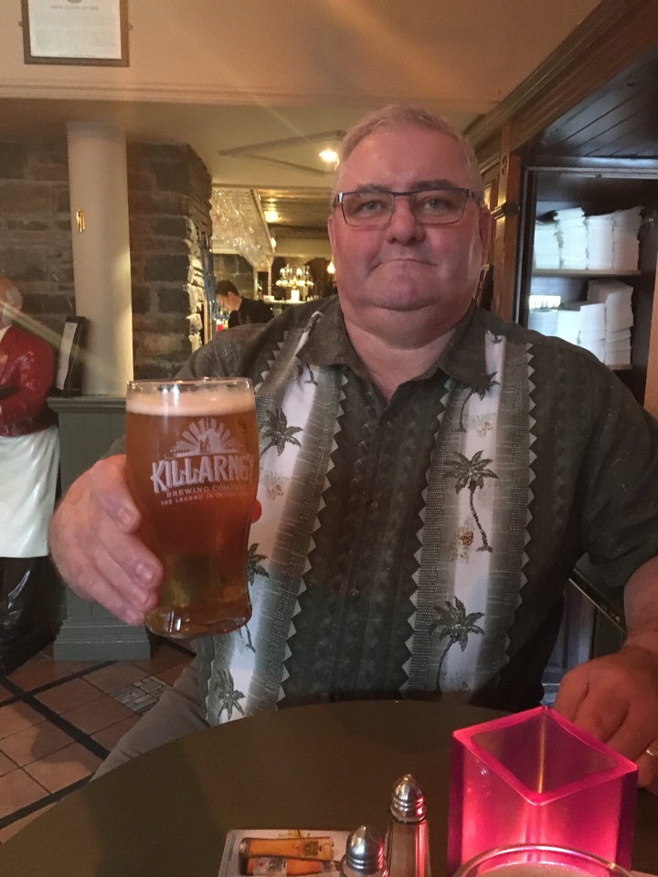 Homme tenant un verre de bière dans un cadre intérieur.
