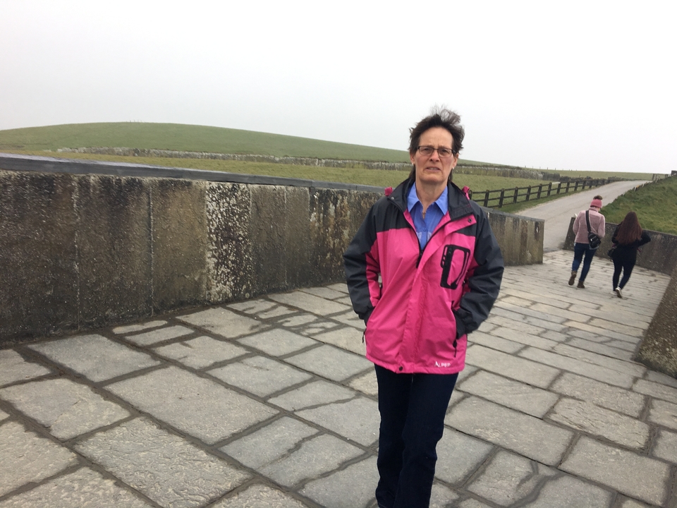 Femme marchant sur un sentier de pierre sous un ciel nuageux.
