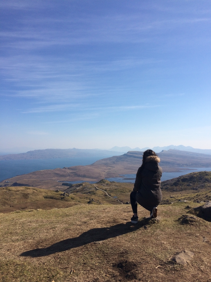 Person gazing at a serene landscape with hills and water.