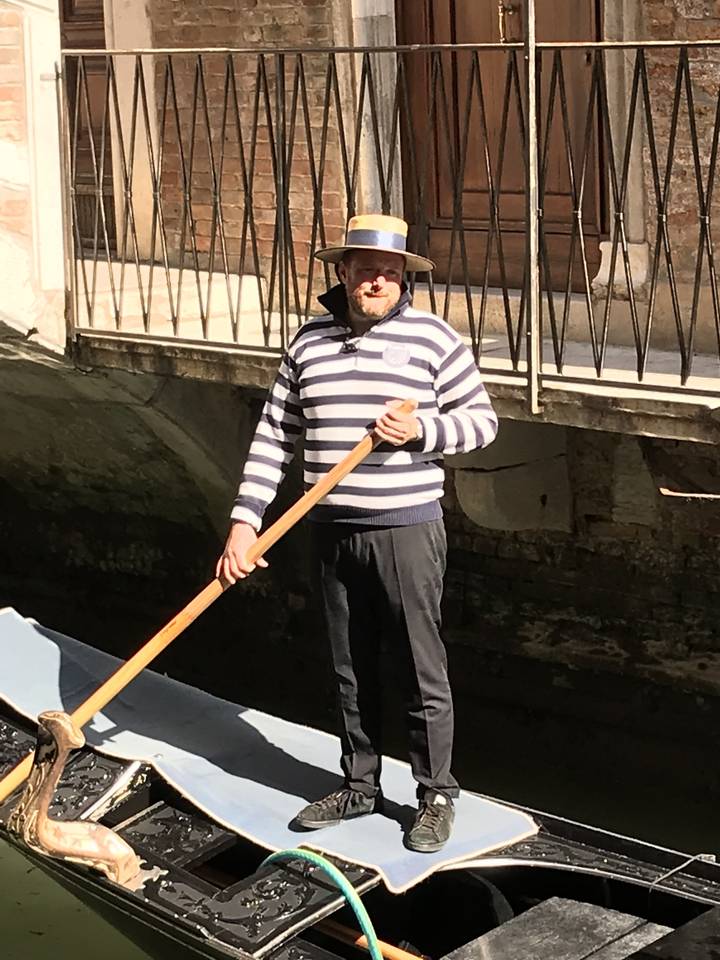 Gondolier debout dans une barque sous un pont.