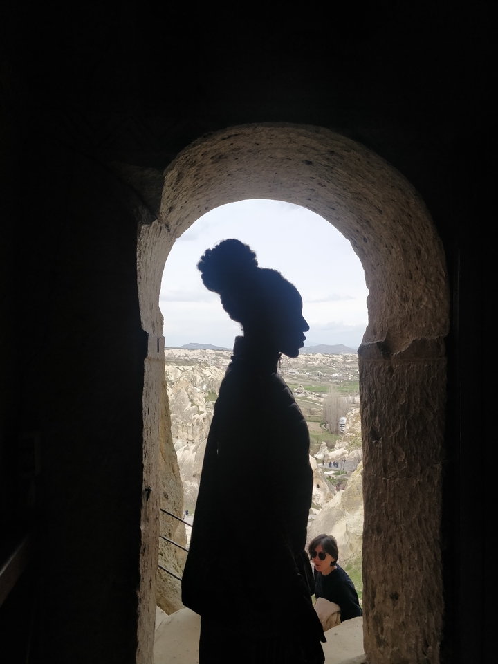Silhouette d'une personne dans une fenêtre en arc donnant sur un terrain rocheux.