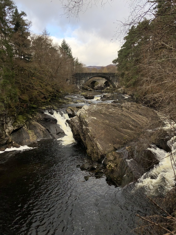 Rocky river with waterfalls and an arched bridge.